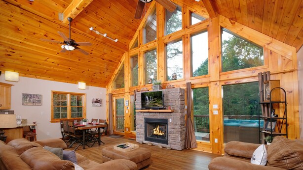 A spacious living room with a fireplace, leather sofas, wooden floors, and large windows offering views of the outdoors.