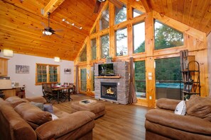 Relax in a warm and inviting cabin with a stone fireplace, comfortable seating, and expansive forest views.