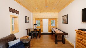 A cozy living room with a brown leather couch, a wooden coffee table, and a pool table. There is a sign that reads "FAMILY" on the wall.