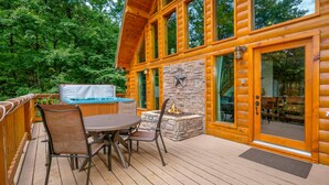 A wooden deck with a hot tub, stone fireplace, and a dining table with chairs.