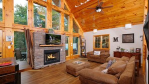 A spacious living room with a stone fireplace, leather sofas, and large windows offering a view of the outdoors.