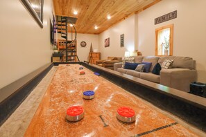 A shuffleboard table with pucks, a sofa, and a staircase in a room with wooden ceilings and a 'FAMILY' sign.