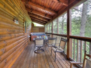 A wooden cabin with a covered porch, a hot tub, and outdoor seating. - 6BR close to PF Parkway- 2 hot tubs, game room, 4 decks, 3 living areas! (Pigeon Forge)