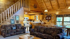 Un intérieur de chalet chaleureux comprenant un salon, un coin repas, une cuisine et un escalier.
