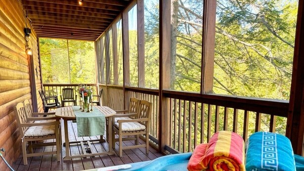 Une terrasse en bois avec un jacuzzi, des chaises et une table agrémentée d’un vase de fleurs.