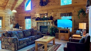 Un intérieur de chalet chaleureux avec un plafond en bois, une cheminée, un téléviseur et un coin repas.