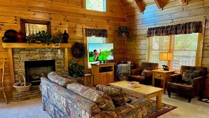 L’intérieur d’un chalet accueillant, avec une cheminée en pierre, un téléviseur, un canapé et une table basse.