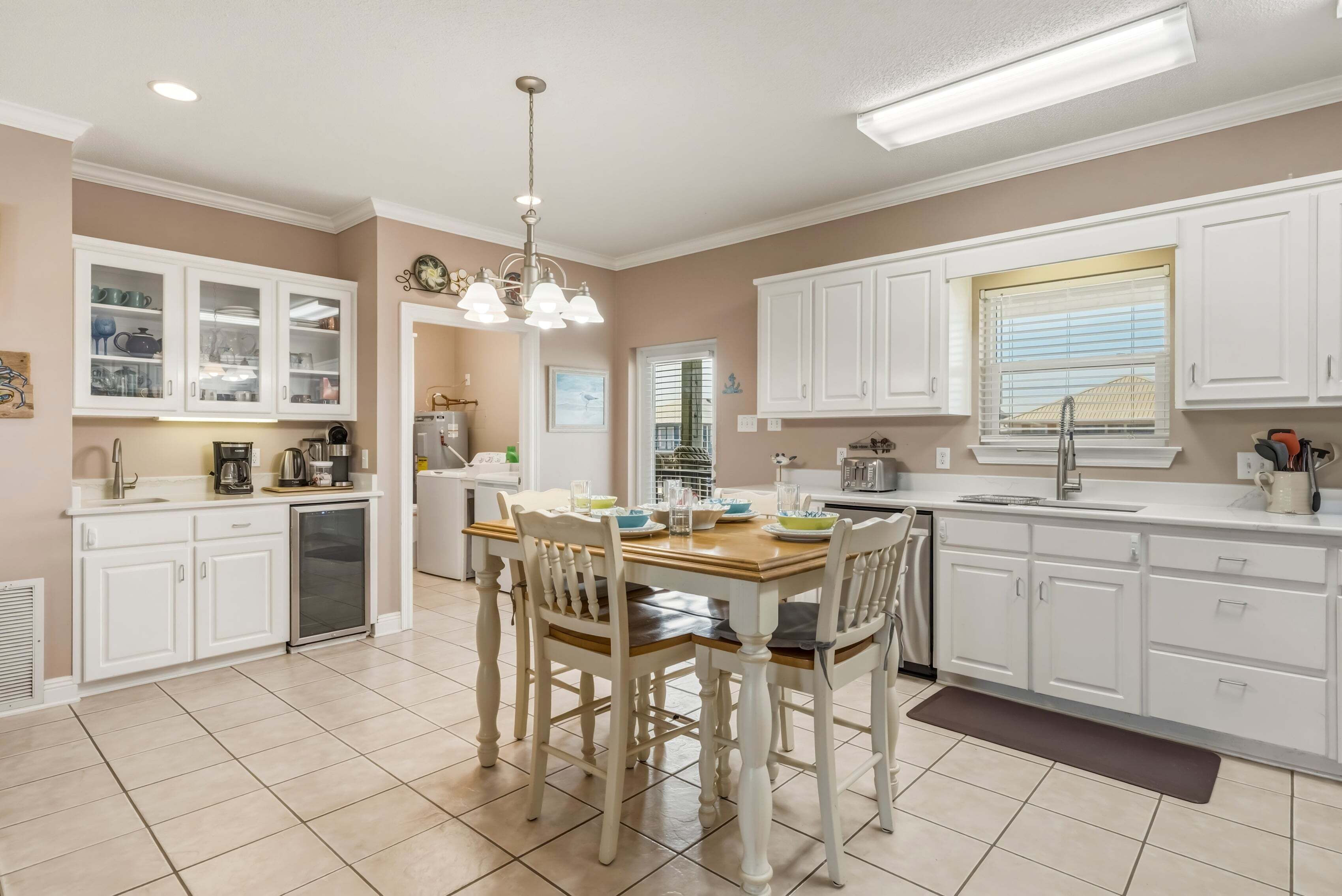 A kitchen with white cabinets, a dining table with chairs, a refrigerator, and a window with blinds.