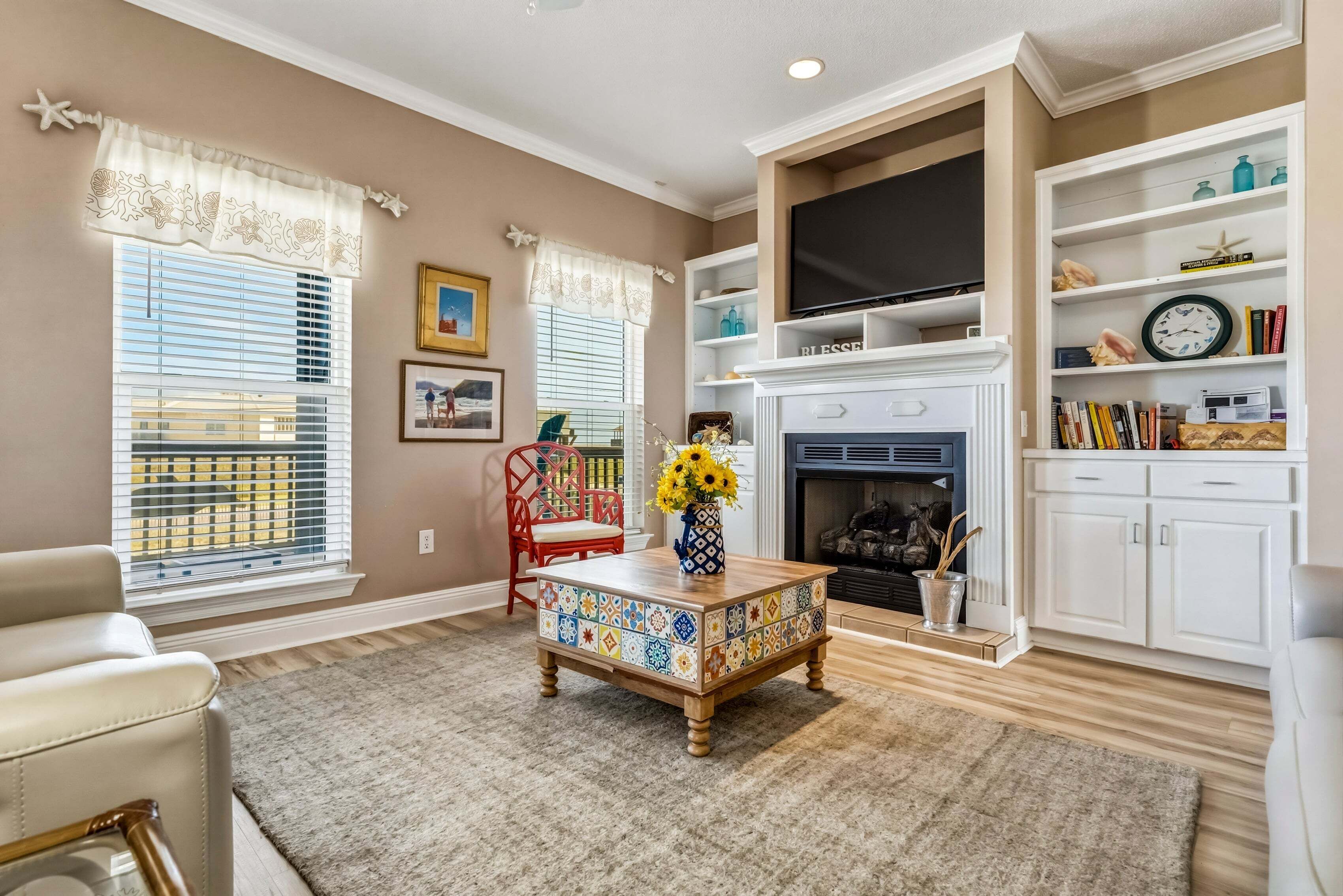 A living room with a fireplace, a television, a bookshelf, and a patterned coffee table.