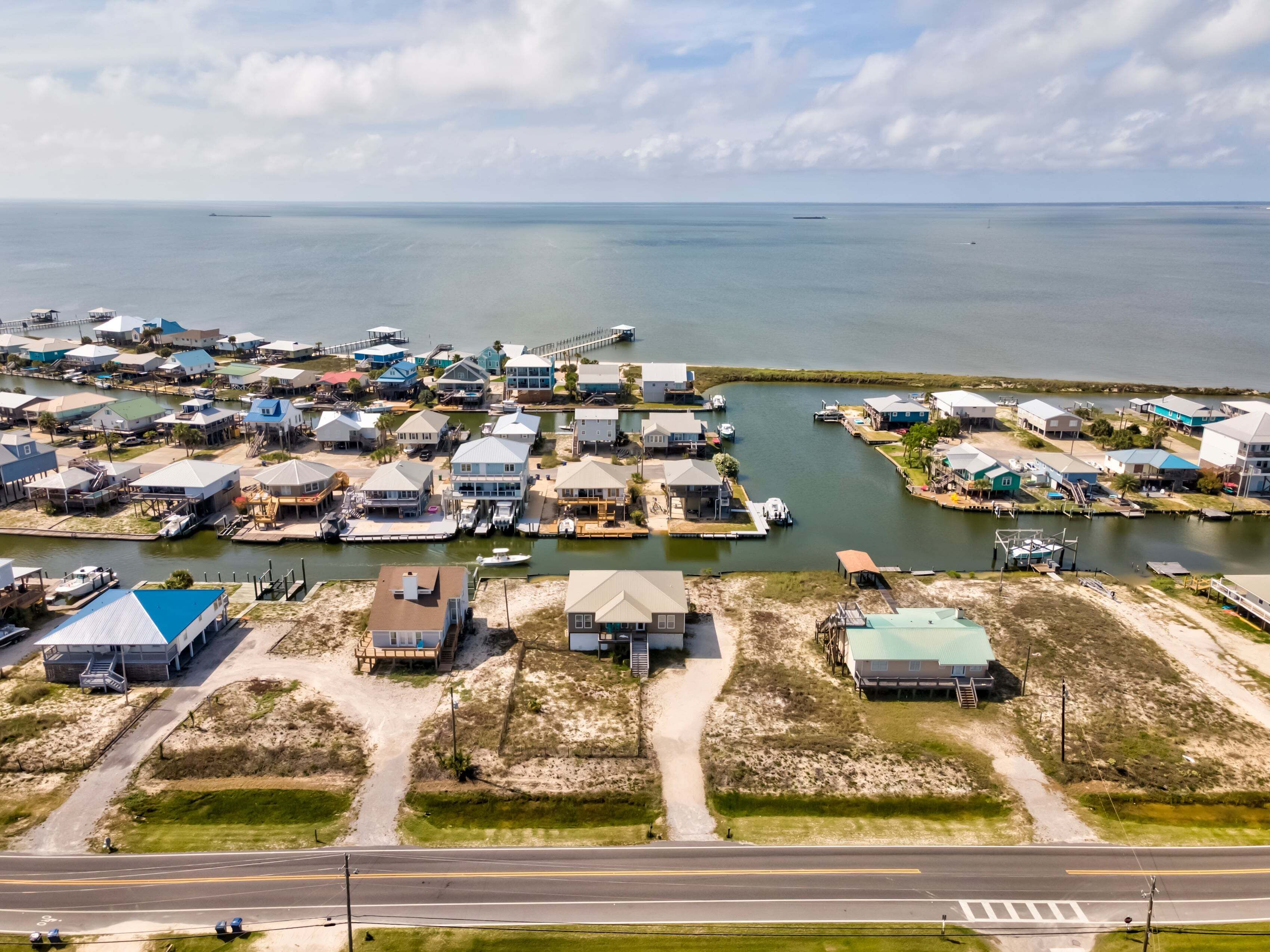 An aerial view of a coastal residential area with houses, docks, and a road.