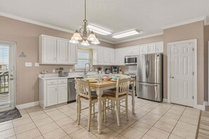 Una cocina con armarios blancos, un refrigerador de acero inoxidable, un microondas y una mesa con sillas.