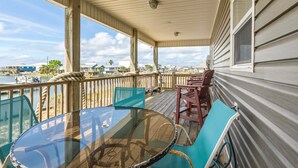 A covered outdoor area with a glass table and chairs, a wooden deck, and a view of the water and buildings.