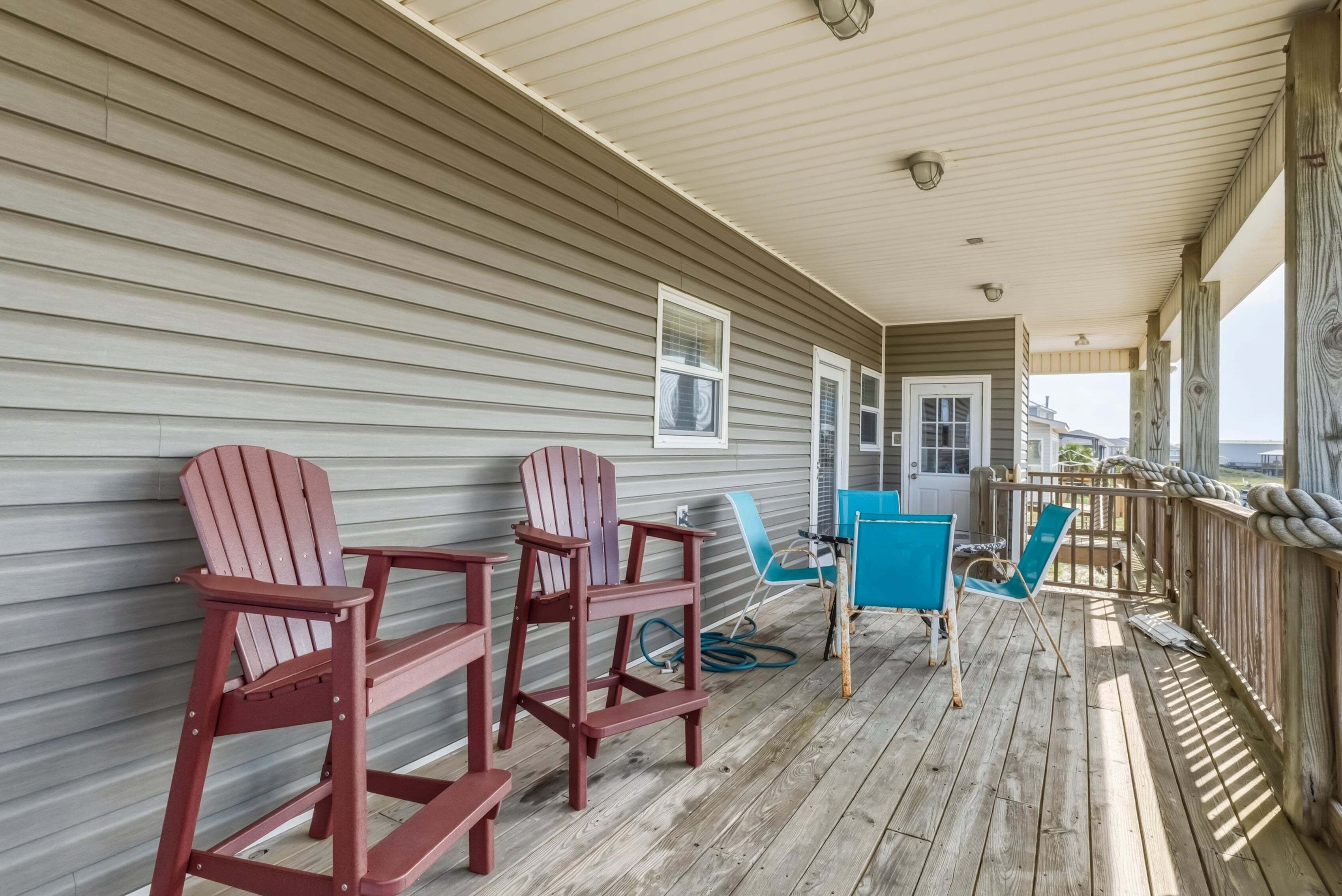 A covered porch with Adirondack chairs, a blue folding chair, and a wooden deck.