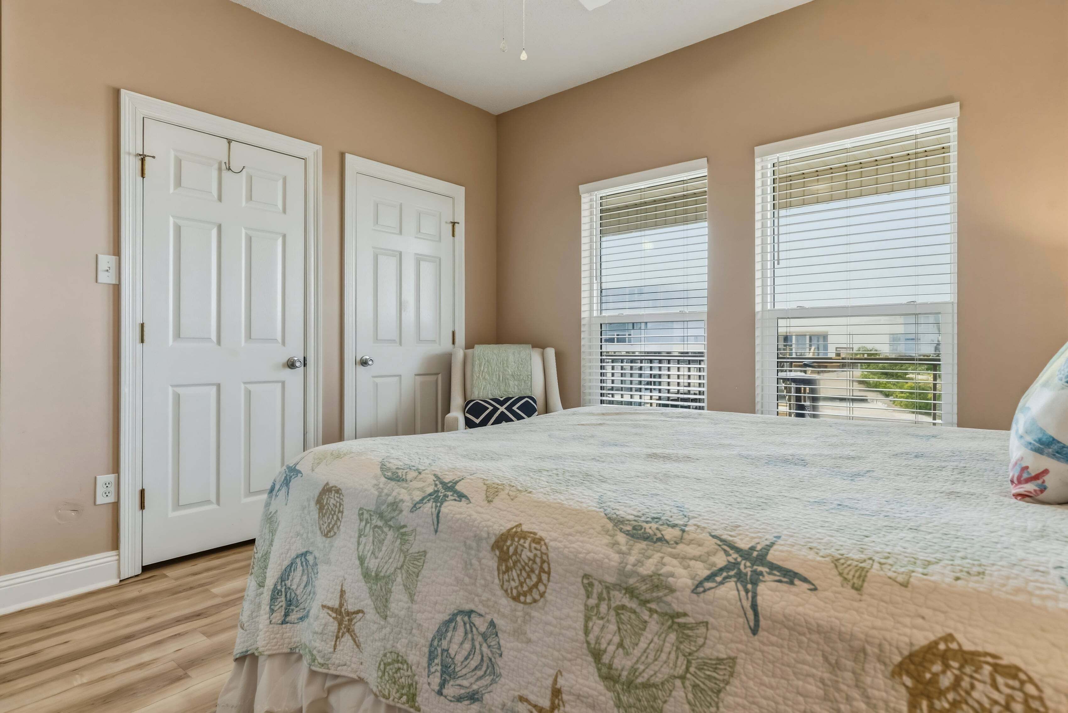 Une chambre à coucher avec un lit, deux portes blanches, une fenêtre avec des stores et une vue sur un balcon.