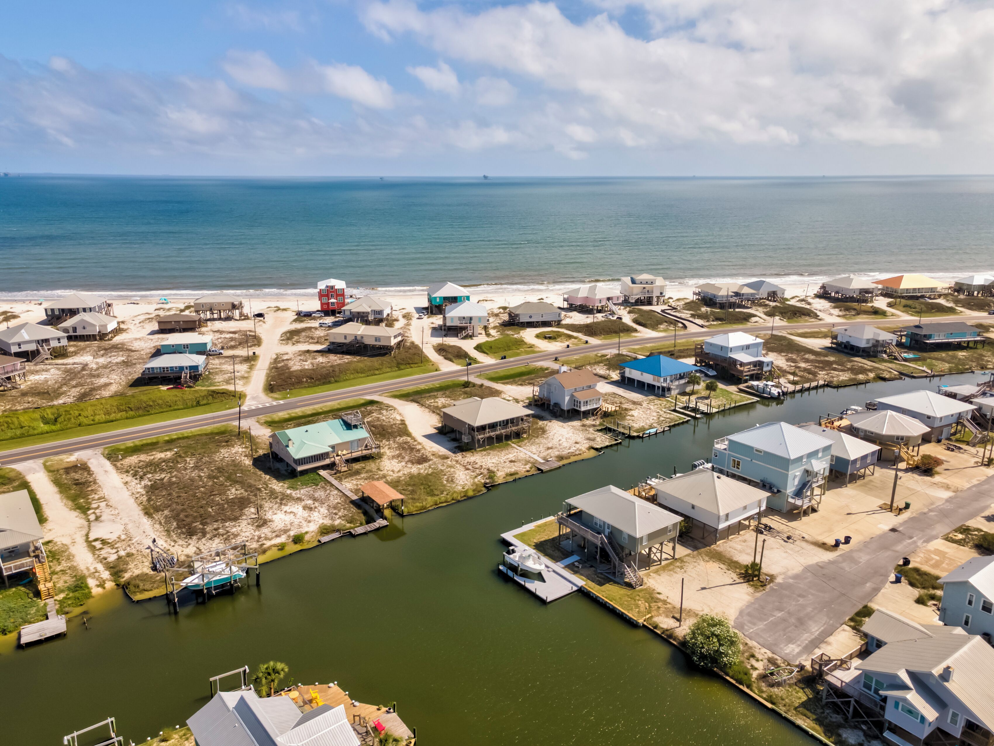 An aerial view of a coastal residential area with houses, a marina, and a road.