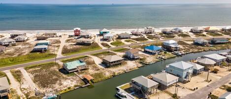 An aerial view of a coastal residential area with houses, a marina, and a road.