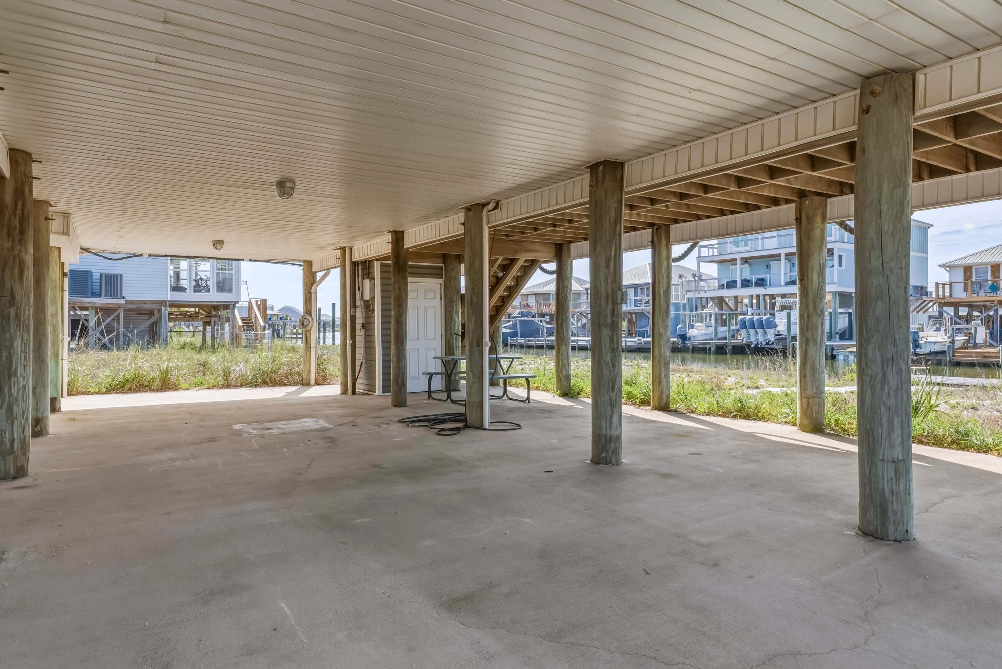 Una estructura al aire libre, cubierta, con piso de concreto, vigas de madera y vista a edificios residenciales al fondo.