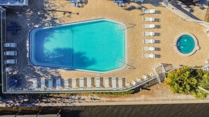 Luftaufnahme eines Resorts mit einem rechteckigen Schwimmbecken, einem kleineren kreisförmigen Pool und Liegebereichen mit Sonnenliegen.