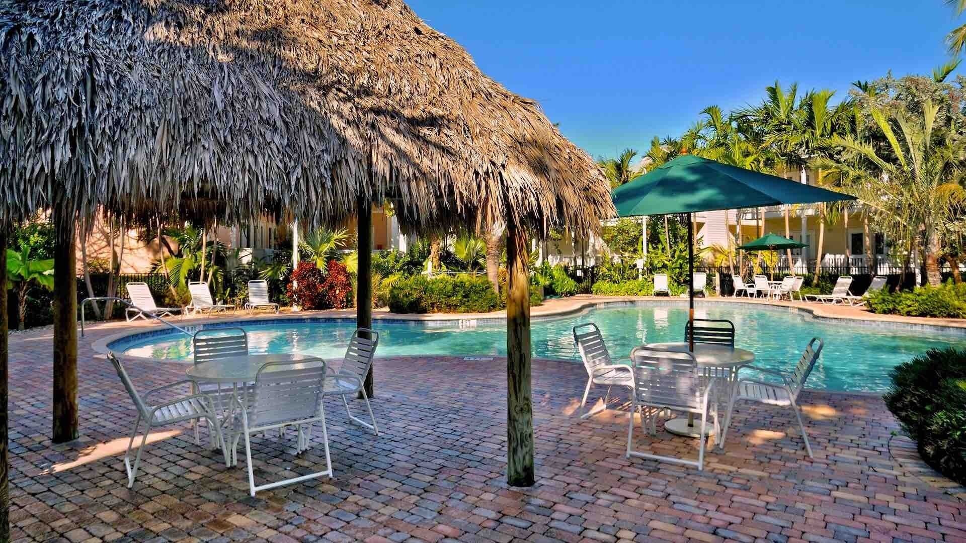 Un espace piscine doté de chaises longues et d’une structure recouverte d’un toit de chaume.