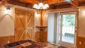 A bedroom with a large bed, wooden ceiling beams, a sliding glass door to a balcony, and a quilted bedspread.