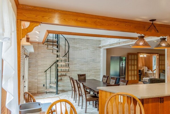A modern kitchen with a wooden countertop, a dining area with a large table and chairs, and a spiral staircase leading to an upper level.