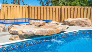 A swimming pool with a wooden fence, large rocks, and a blue border.