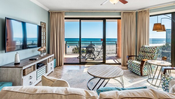 A spacious living room with a large flat-screen TV, a ceiling fan, and a balcony with a view of the ocean. - Mesmerizing Views in this Gulf Front Condo! (Orange Beach)