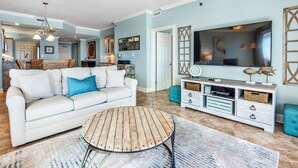 A living room with a white sofa, a wooden coffee table, a TV, and a kitchen in the background. - Mesmerizing Views in this Gulf Front Condo! (Orange Beach)