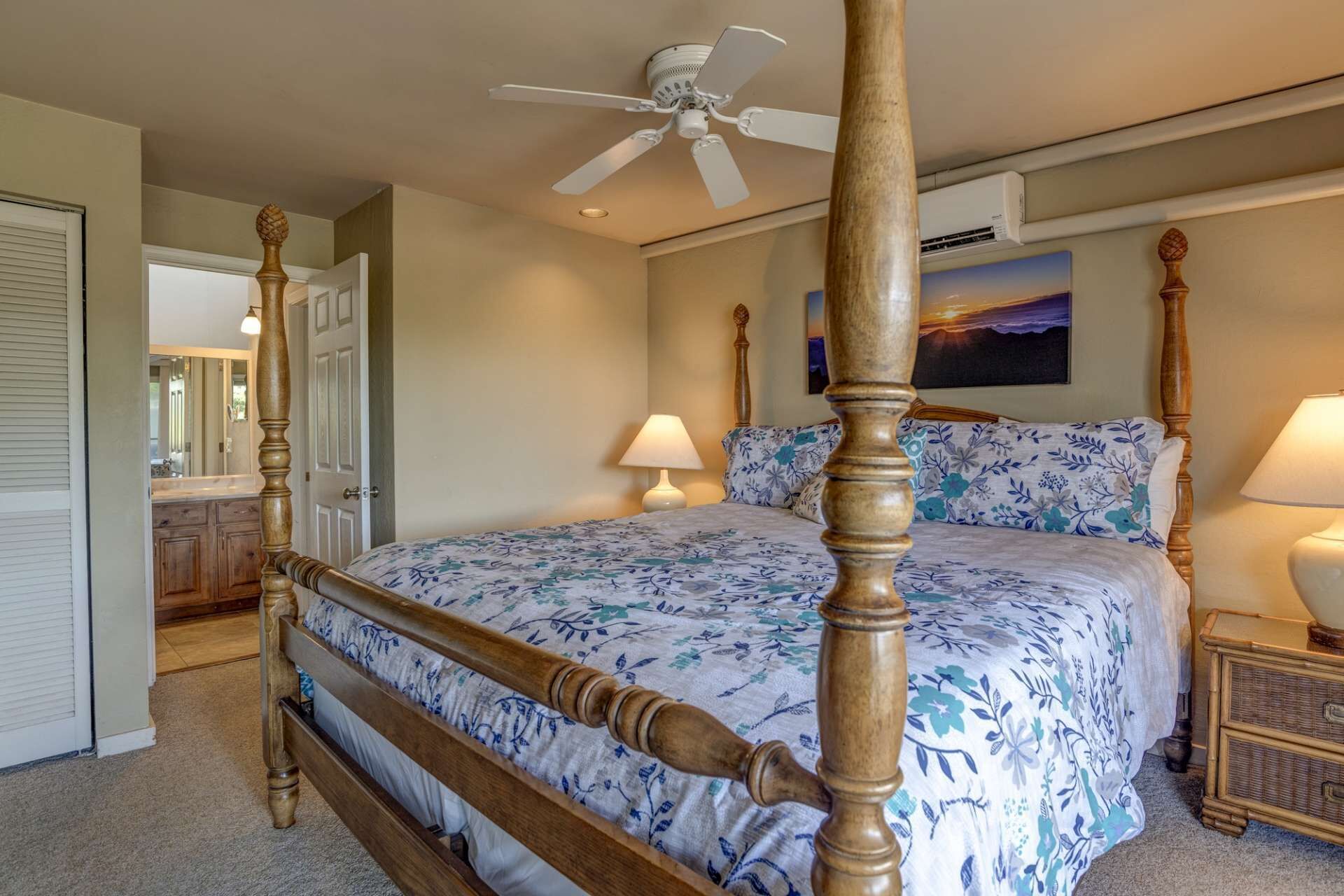 A four-poster bed with a floral bedspread, two bedside lamps, and a ceiling fan in a hotel room.