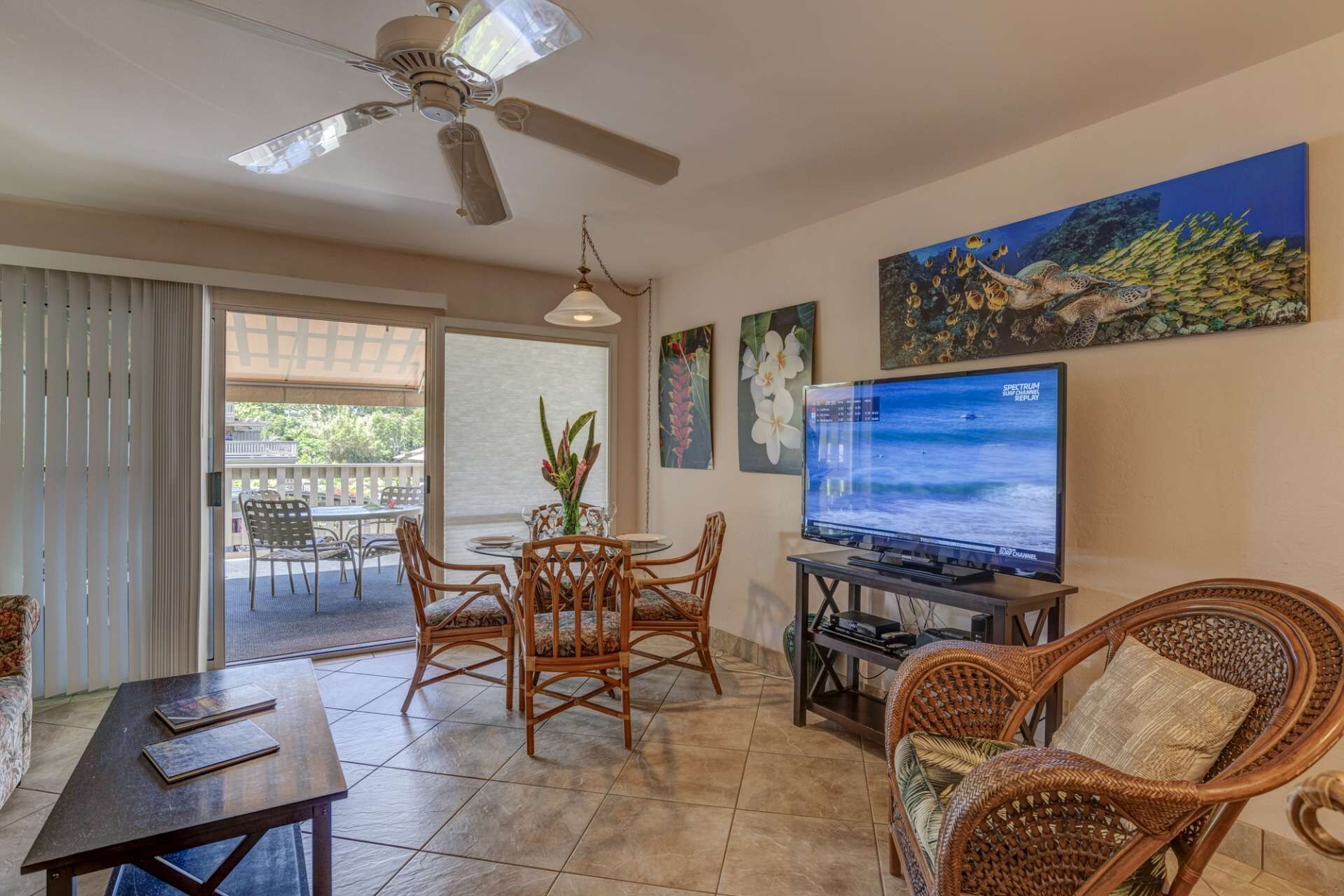 A living room with a television, wicker furniture, and a ceiling fan.