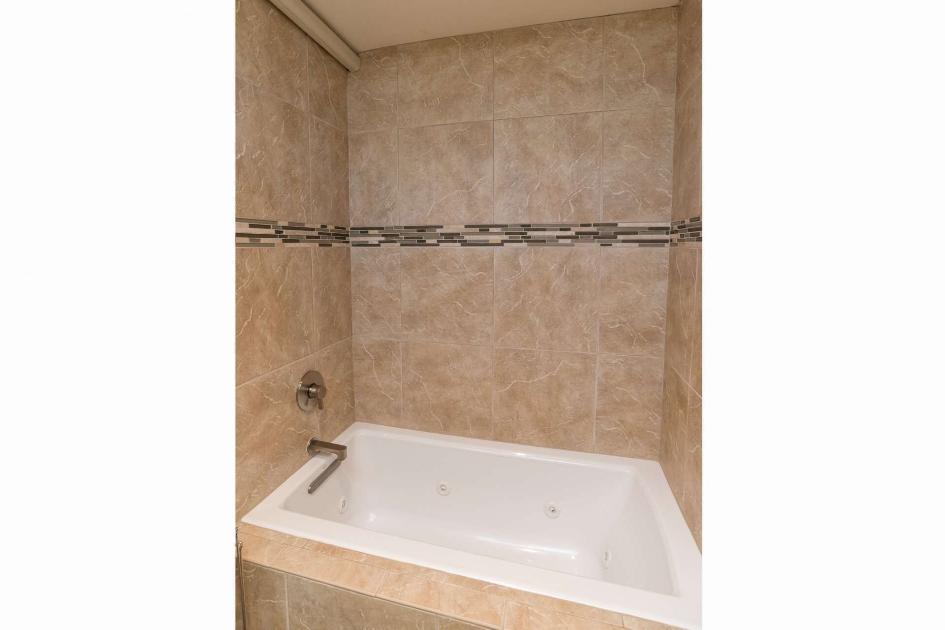 Une salle de bain avec une baignoire, des murs carrelés et un espace douche.