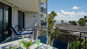 A balcony with a table set for dining, overlooking a pool and palm trees. - **FOLLOW THE SUN** Ocean Condo / Pool & Tennis + Last Key White Glove Service... (Key West)