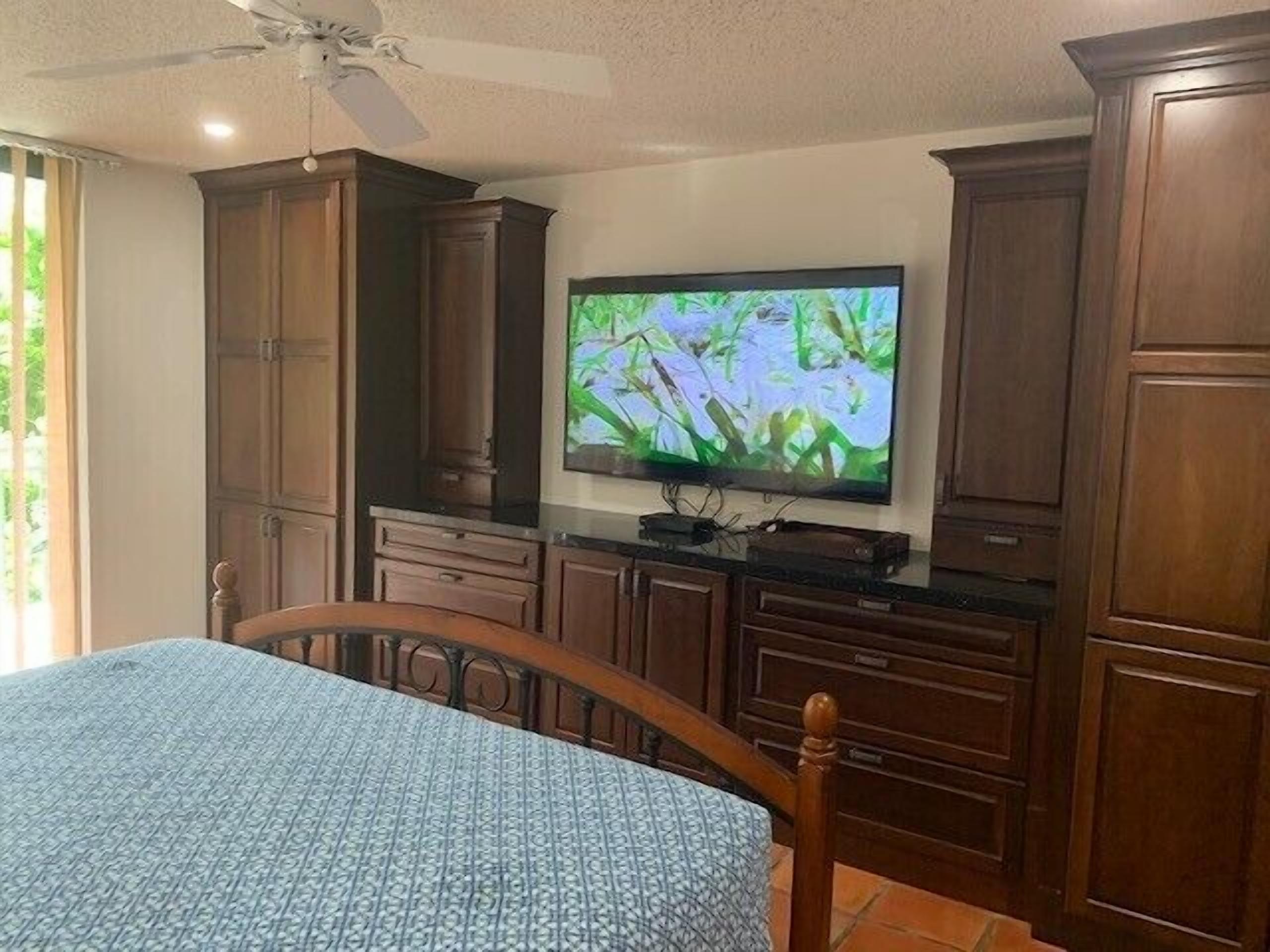 A bedroom with a bed, wooden cabinets, a television, and a ceiling fan.