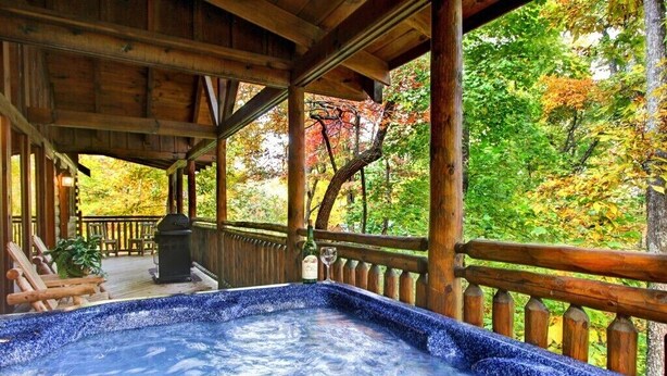 A wooden deck with a hot tub, surrounded by a wooden fence and trees with autumn foliage.