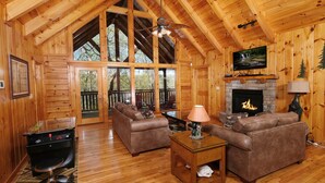 A cozy cabin interior with a fireplace, two sofas, a television, and a ceiling fan.