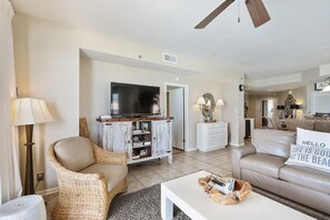 Uma sala de estar com televisão sobre um armário de madeira, uma cadeira de vime, um sofá e uma mesa de centro com revistas.