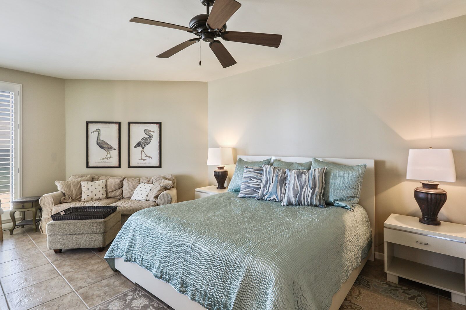 A bedroom with a bed, a nightstand, a lamp, a ceiling fan, a chair, and two wall-mounted lamps.
