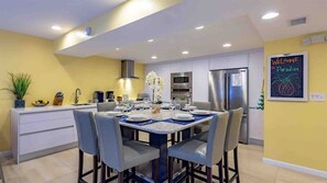 Cocina moderna con comedor, que incluye una isla grande, electrodomésticos de acero inoxidable y un letrero que dice 'Welcome to Paradise'.