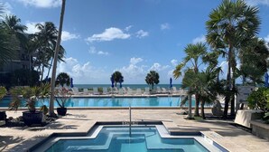 Piscina con vista al océano, rodeada de palmeras y sillones de descanso.