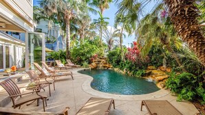 A pool area with lounge chairs and a waterfall feature surrounded by tropical plants.