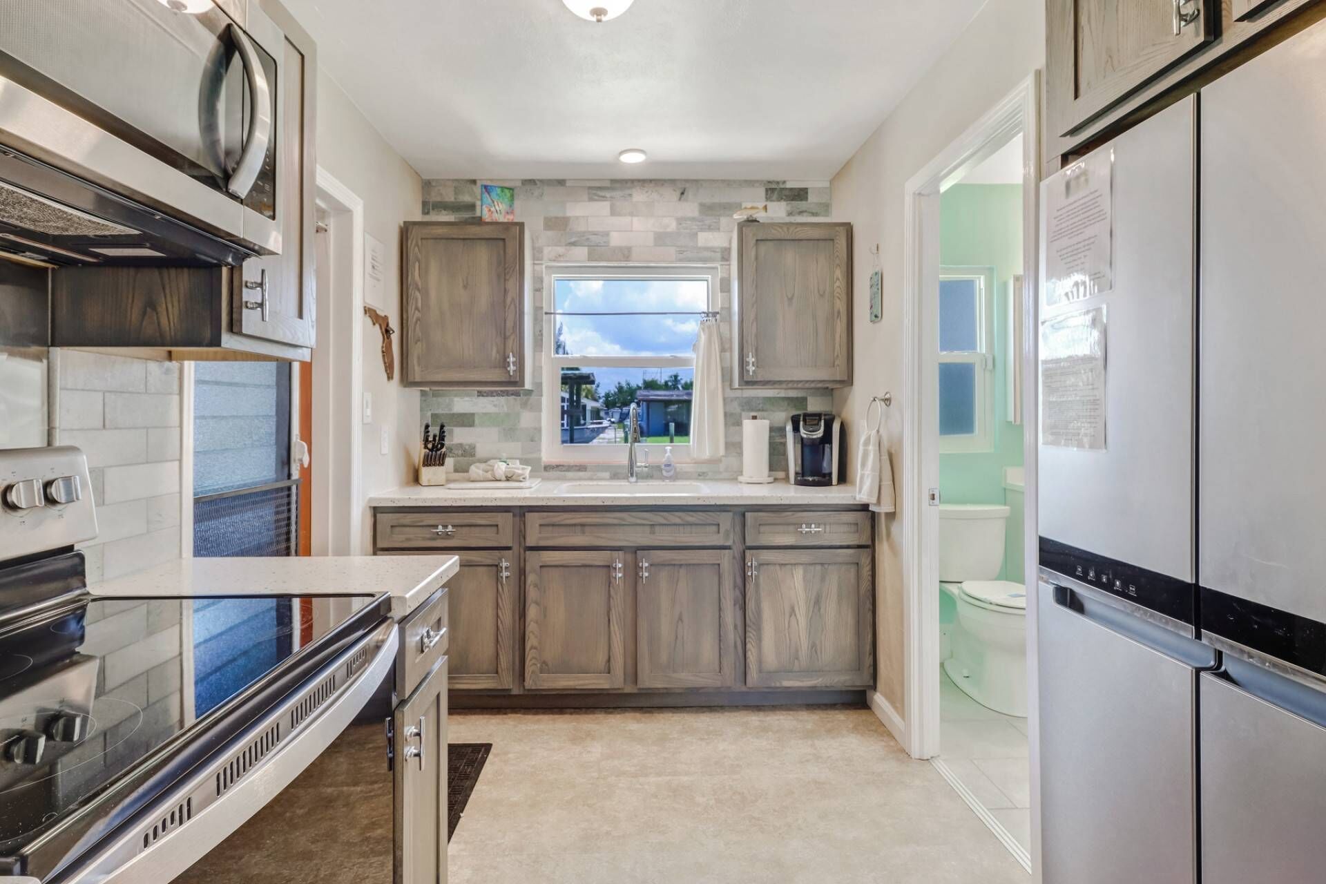 A modern kitchen with a large stove, wooden cabinets, a window, and a refrigerator.