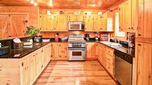 Eine holzgetäfelte Küche im Chalet-Stil mit einer zentralen Kochinsel, Edelstahlgeräten und Holzausstattung.