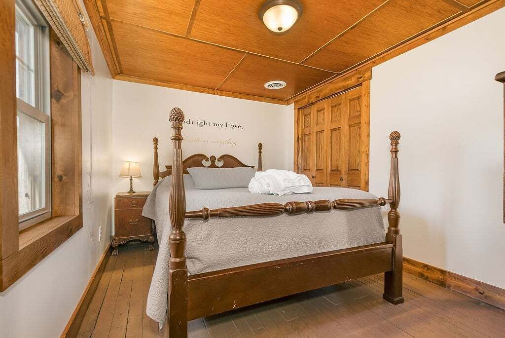 A four-poster bed with a wooden headboard, a bedside table with a lamp, and a wall with a decorative phrase.