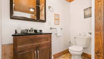 A bathroom with a wooden vanity, a mirror, a toilet, and a hand dryer.