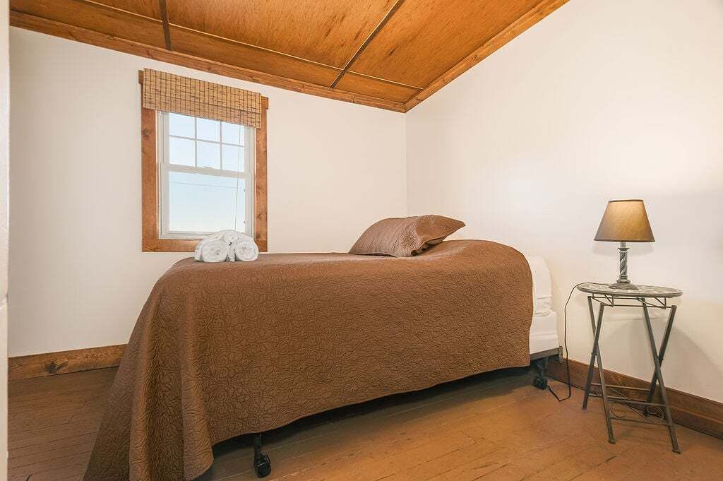 Ein Schlafzimmer mit einem Einzelbett, einem Fenster mit Jalousien, einer Lampe auf einem kleinen Tisch und Holzböden.