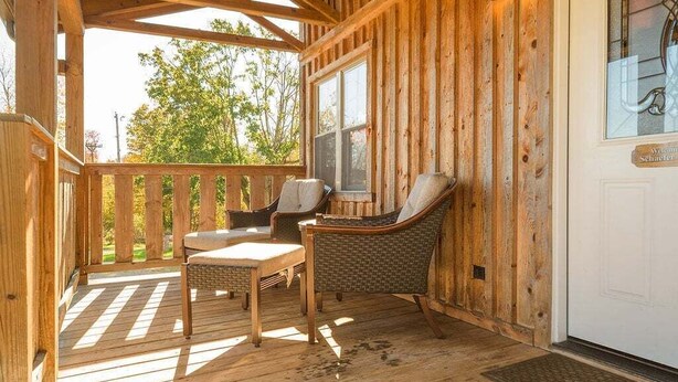 A wooden cabin with a porch, two wicker chairs, a table, and a window. - Schaefer House - Charming Cabin with Orchard Views (Ohiopyle)