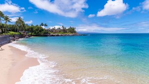 Une plage à l’eau turquoise et limpide, une rive sablonneuse et un bâtiment doté d’un balcon donnant sur l’océan.