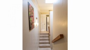 Un couloir étroit avec un escalier recouvert de moquette menant à une pièce dotée d’une porte et d’un luminaire.