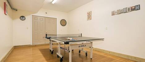 A ping pong table in a room with a door, a dartboard, and a sign that says "PLAY".