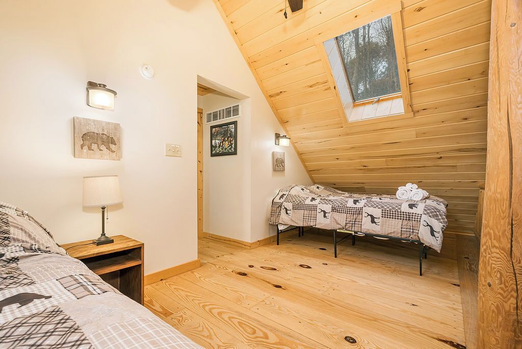A cozy attic bedroom with a sloped ceiling, a bed with a checkered blanket, a bedside lamp, and a small table.